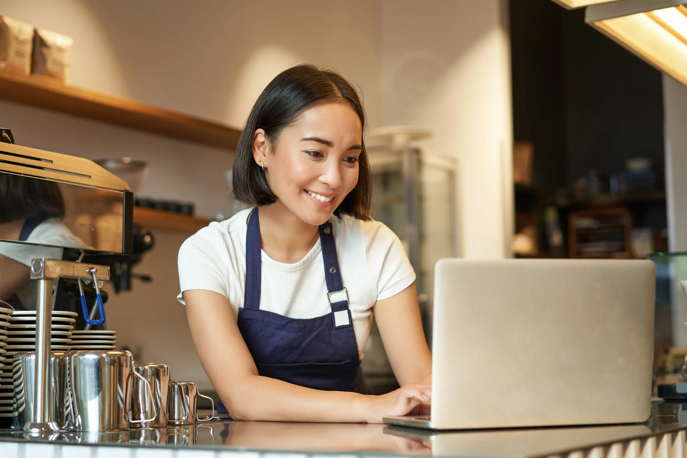A cafe owner working at a laptop behind the counter, processing online orders and customer messages.
